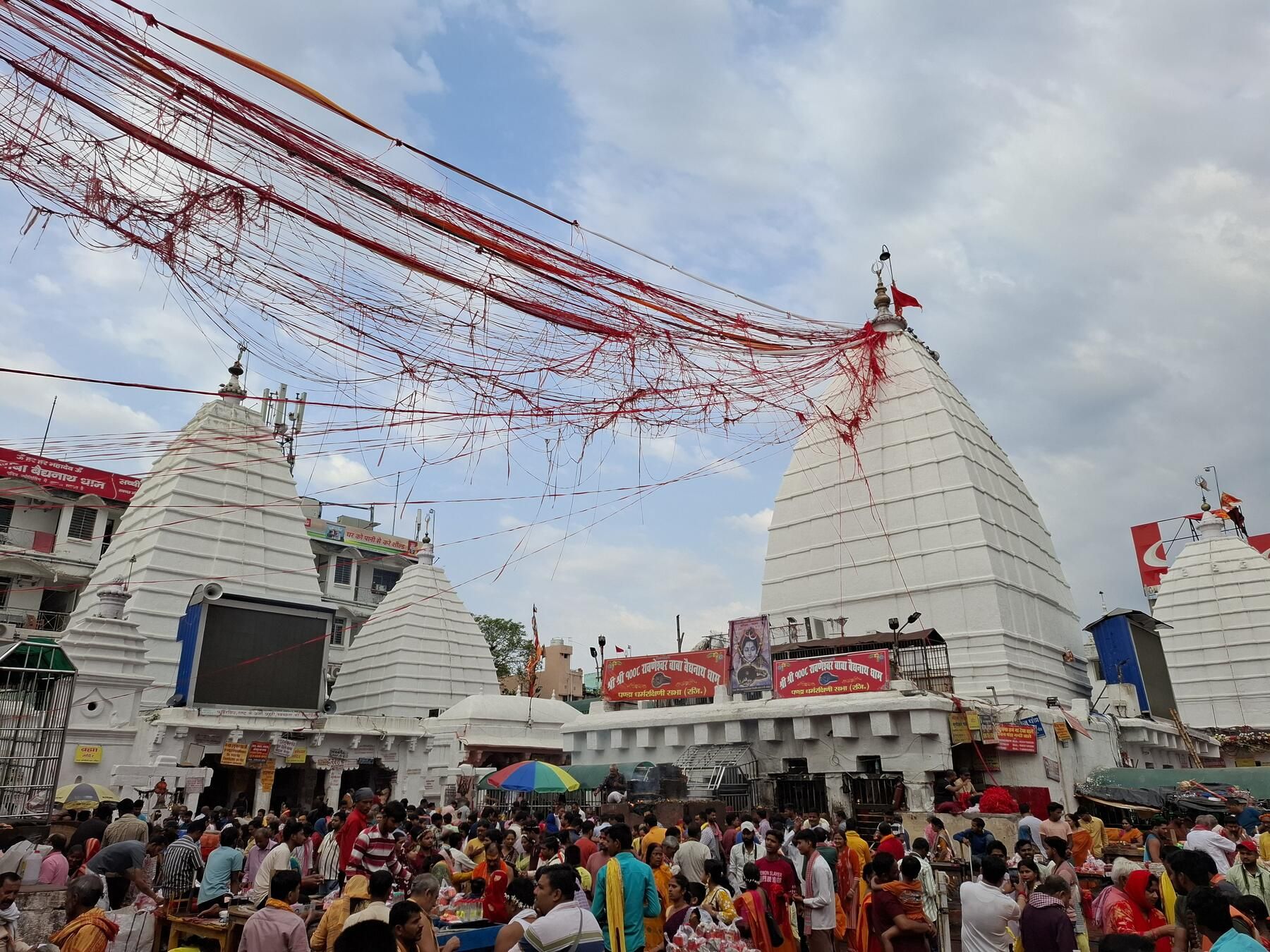 A crowded temple courtyard with several white pyramidal shrines and red threads strung between their tops