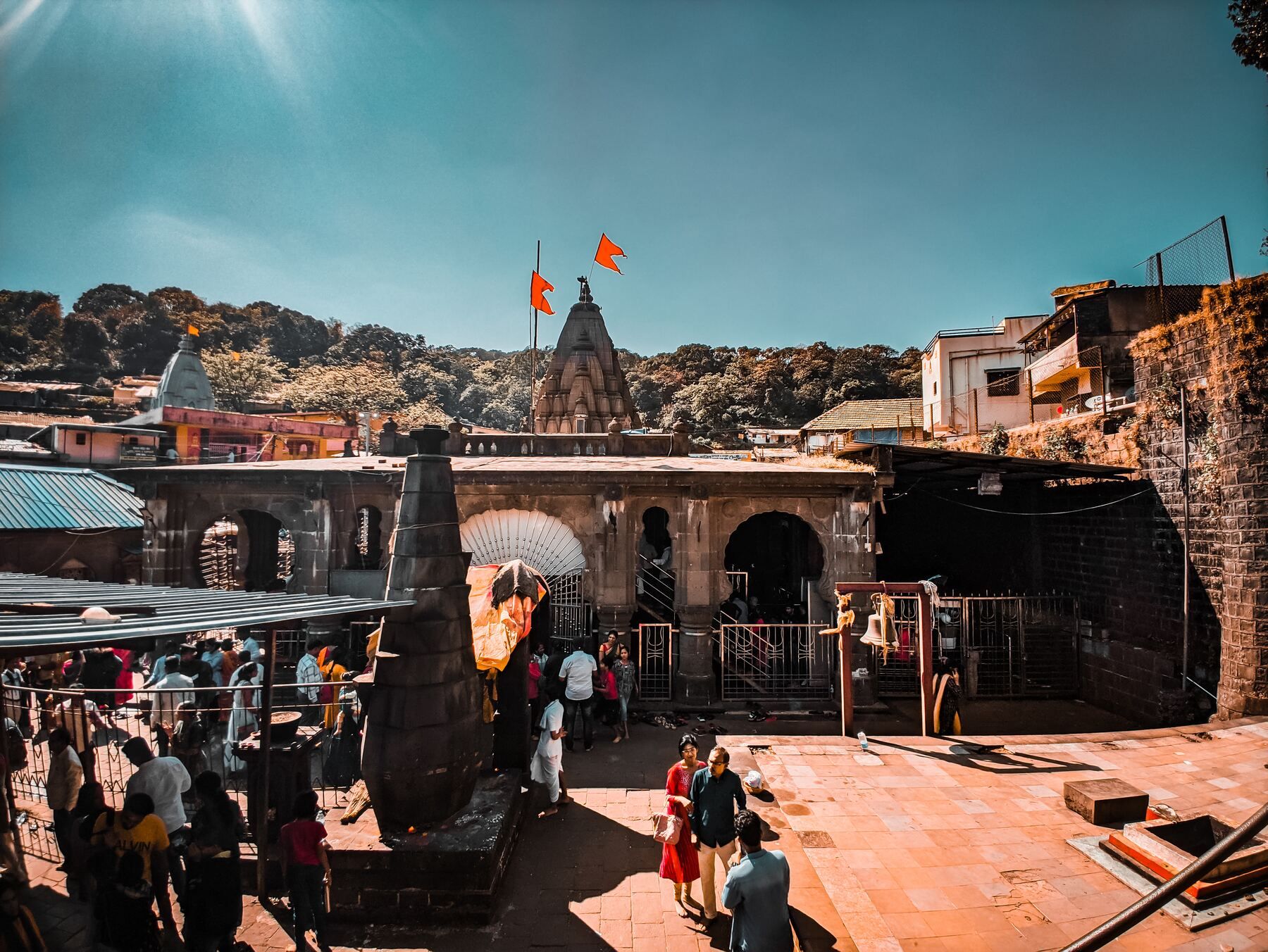 The temple courtyard seen from above, with the stone spire, arched halls, saffron flags and people walking on the paving