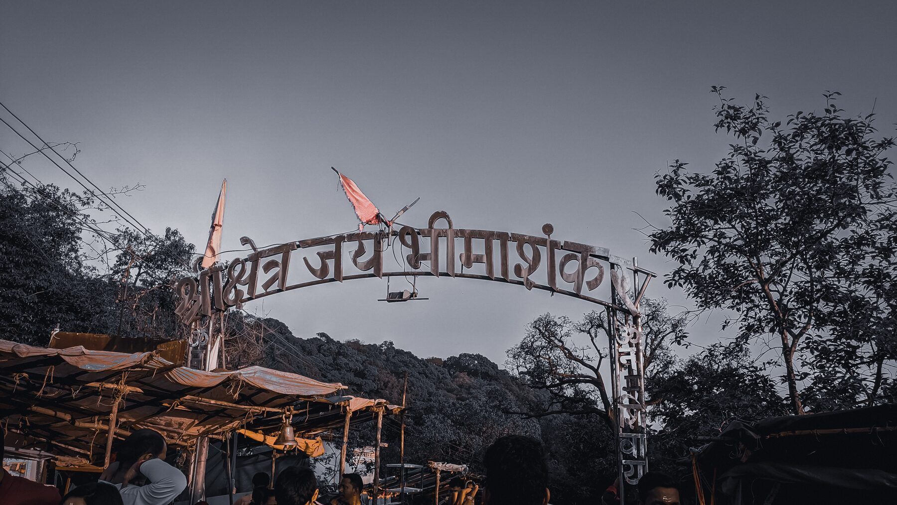 An arch over the path with Devanagari lettering naming Bhimashankar, with stalls and trees on both sides