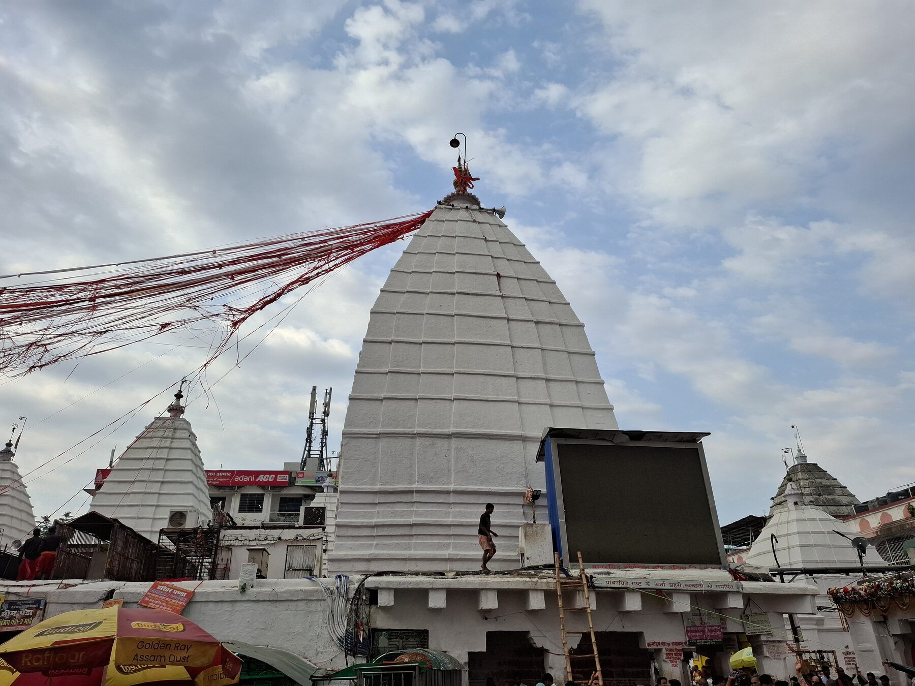 The tall white pyramidal tower of Baidyanath temple under a cloudy sky, with red threads tied from its top and smaller white shrines around it
