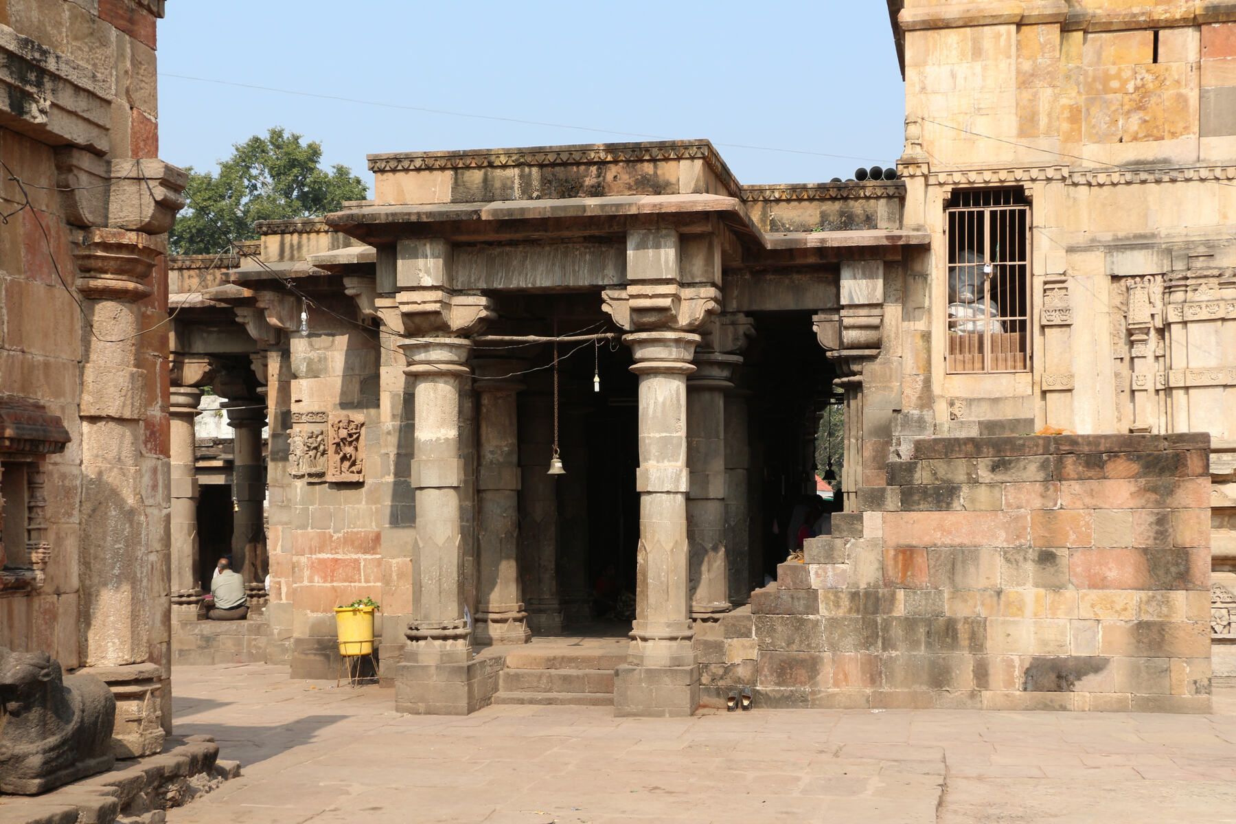 An old stone temple with a pillared porch and carved walls in a paved courtyard