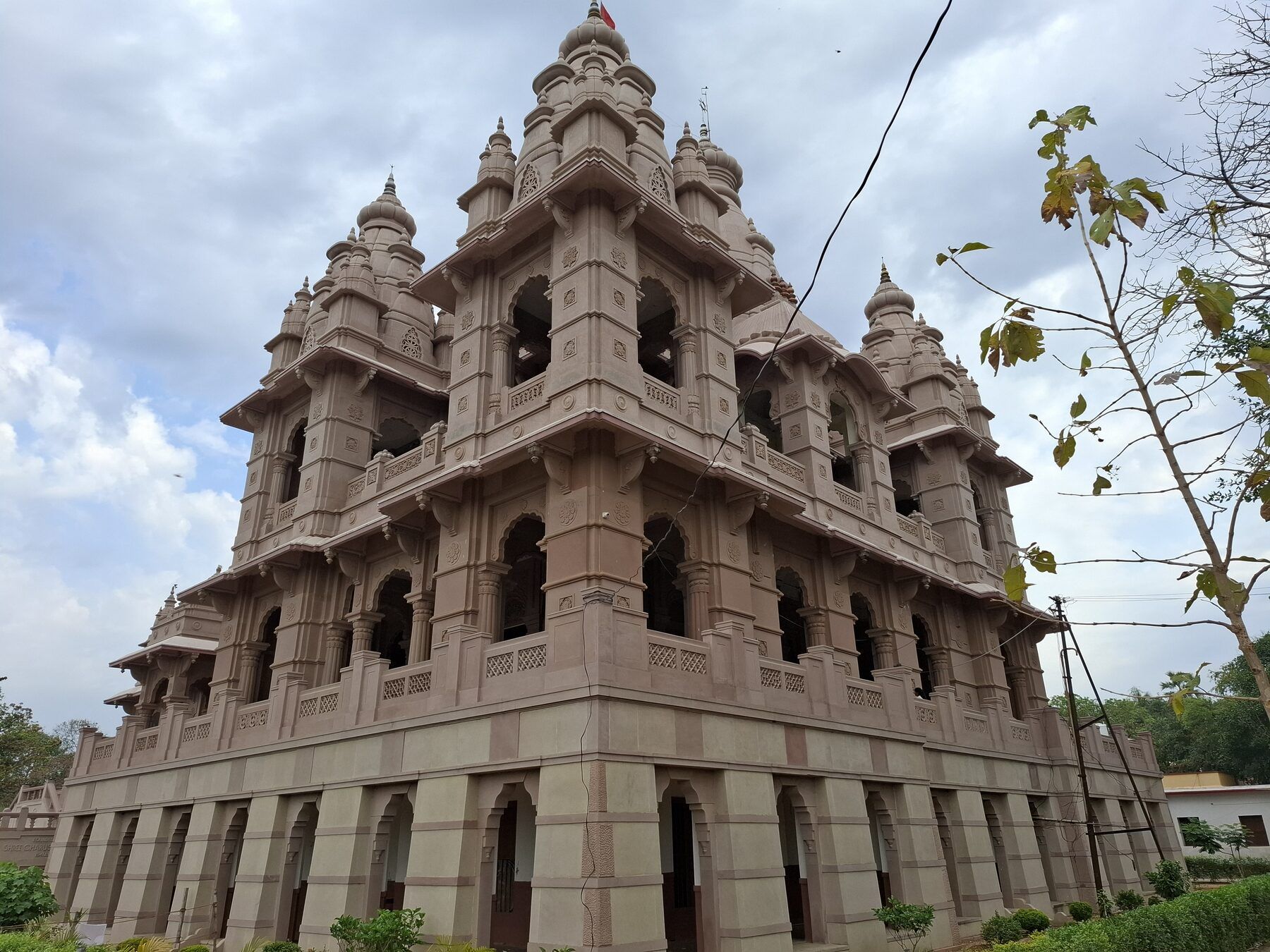 A tall stone temple in a pale reddish tone with tiers of carved towers and arched openings