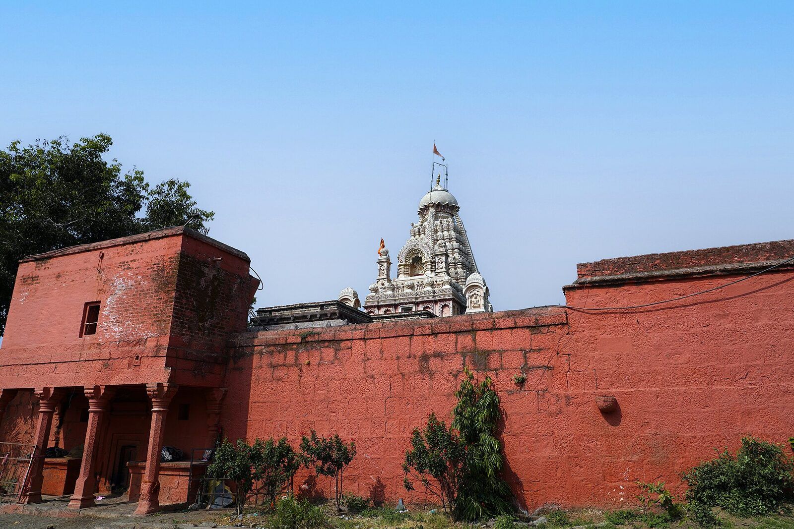 A long red stone wall with a small gatehouse, and the carved temple spire showing above it under a clear sky