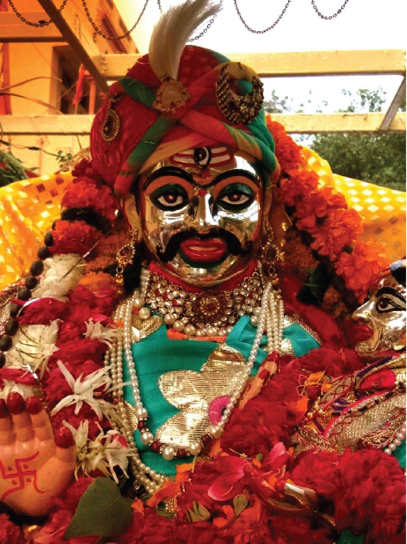 A silver face of Mahakal with a red and gold turban, garlands of flowers and pearl necklaces