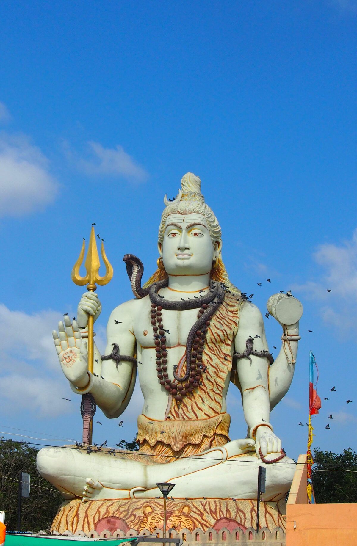 A white statue of a seated Shiva holding a trident, against a blue sky