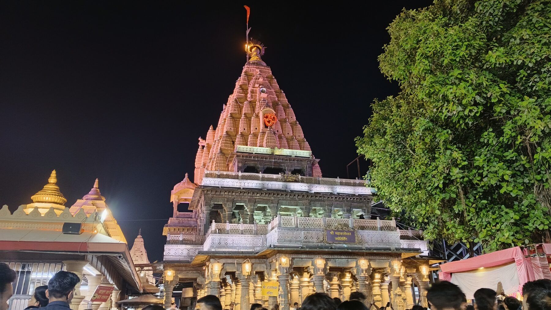 The temple spire lit in pink and gold at night, with a crowd below