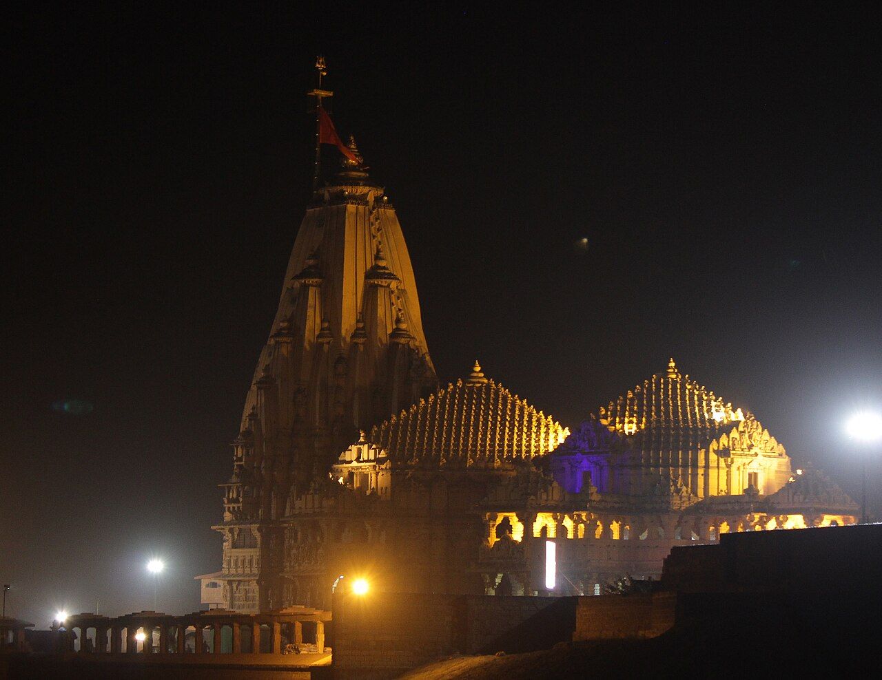 Somnath temple lit in warm light at night, its tall spire and domed halls against a dark sky