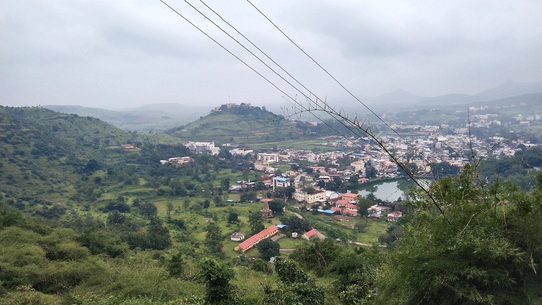A green valley with a small town spread across it and low hills behind, seen from high ground